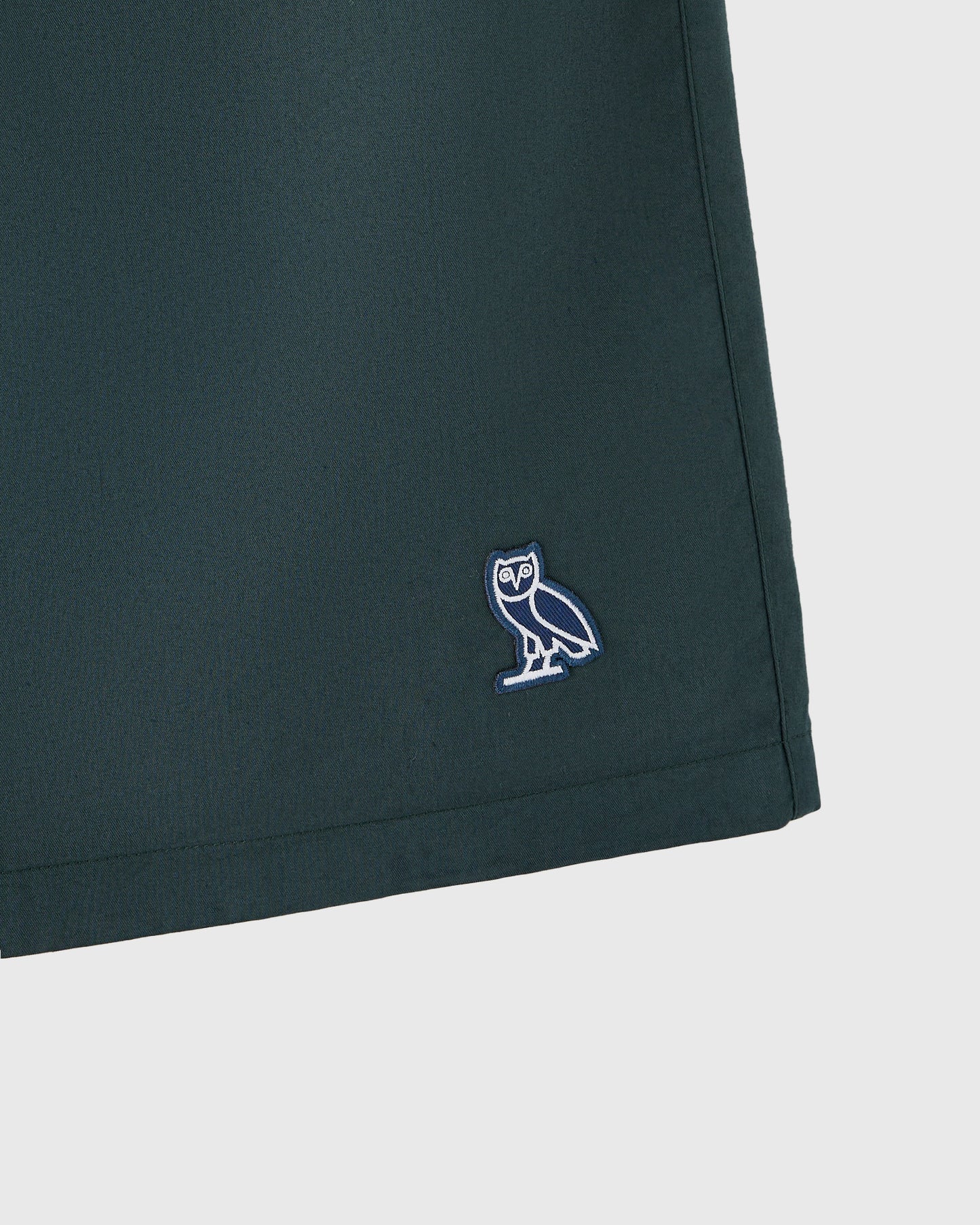 Midnight green camp short with embroidered owl logo on thigh.