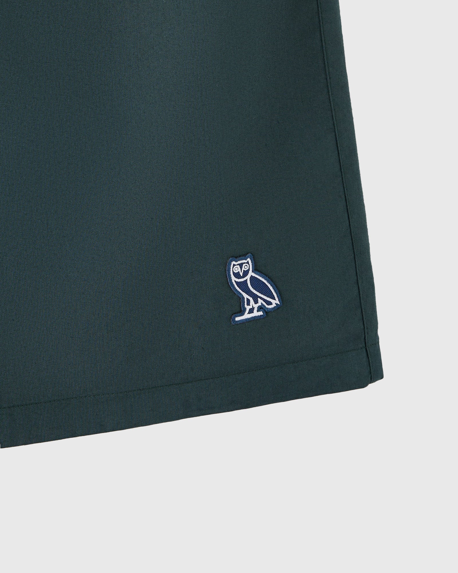 Midnight green camp short with embroidered owl logo on thigh.
