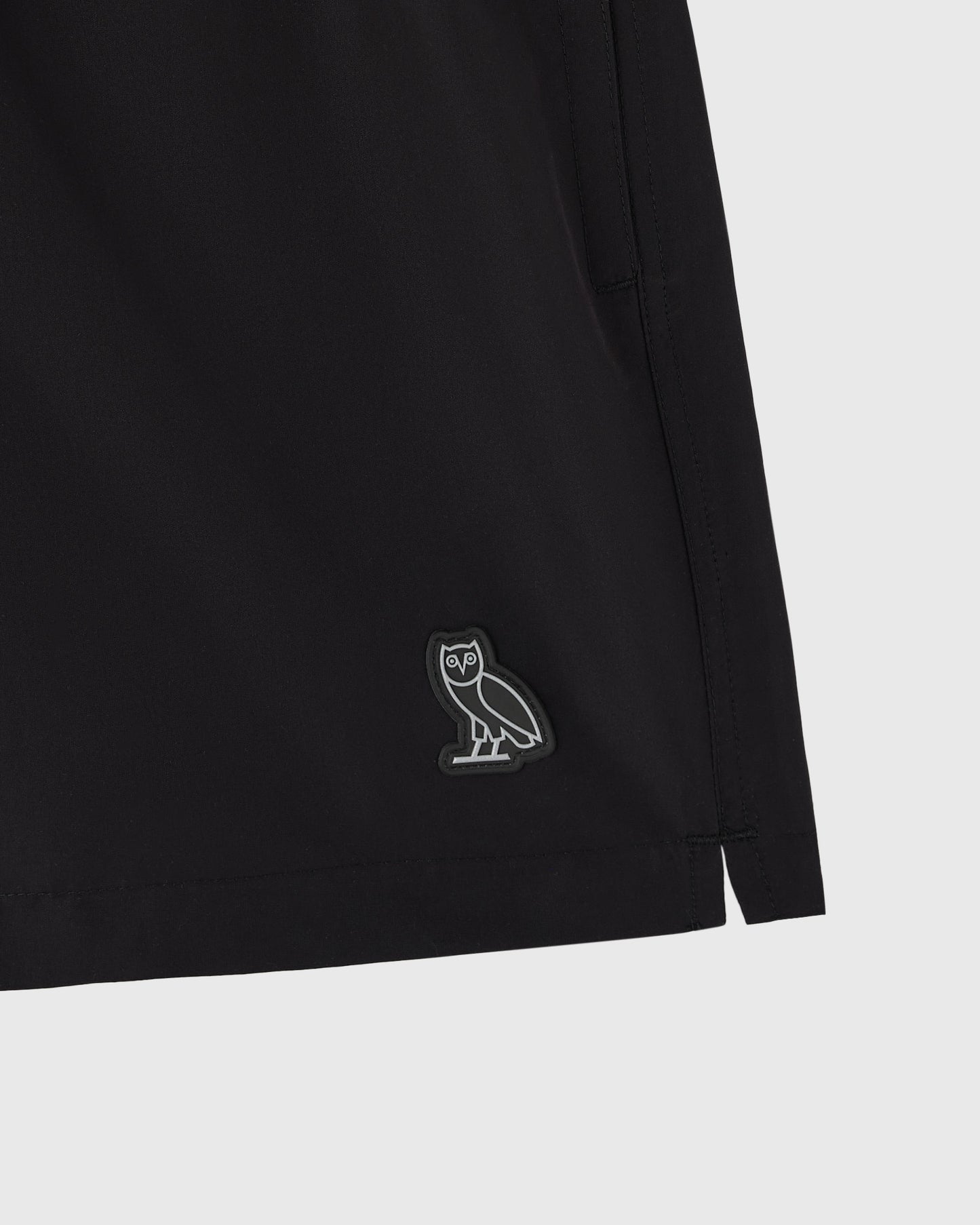 Black swim short with small owl emblem on leg.