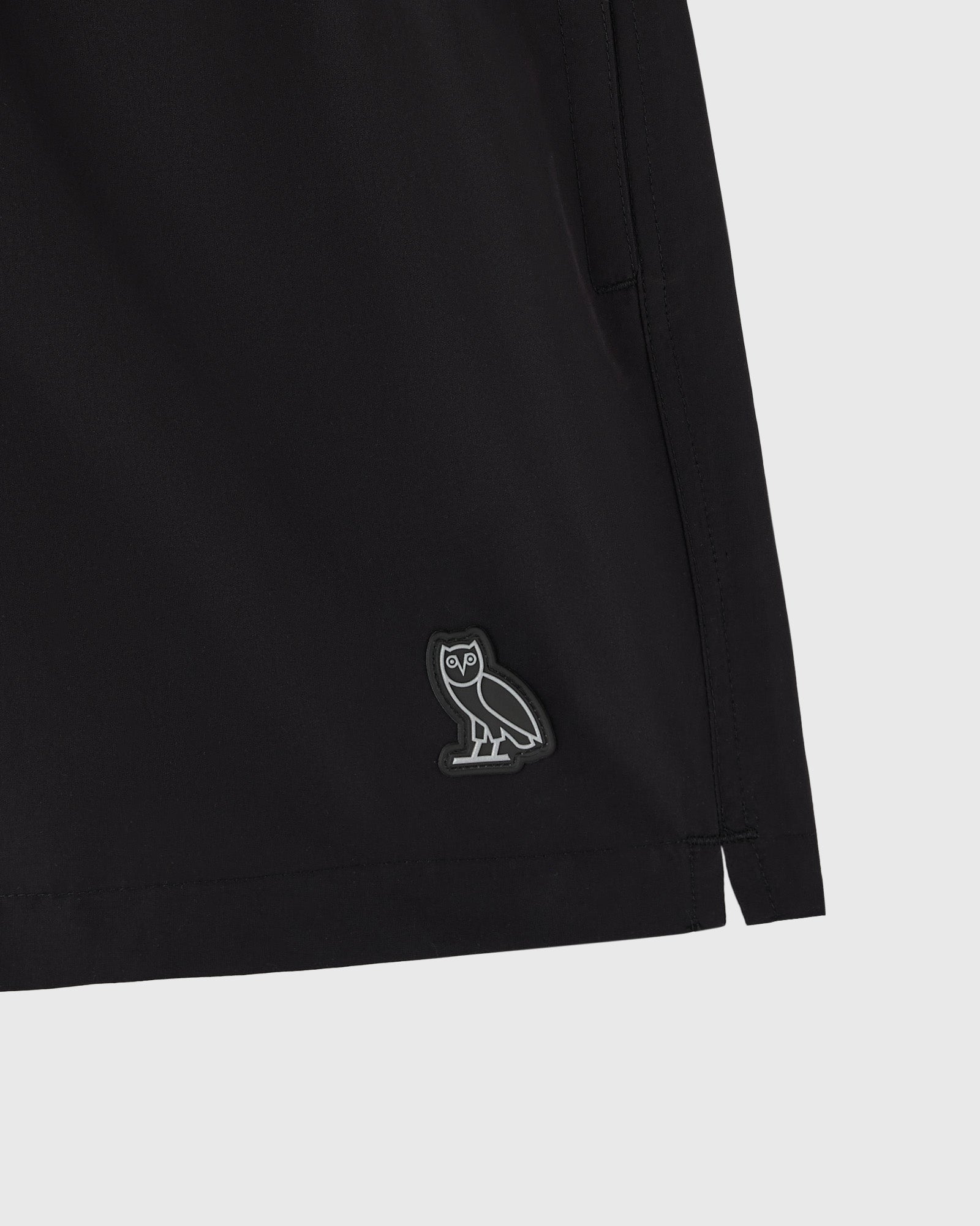 Black swim short with small owl emblem on leg.