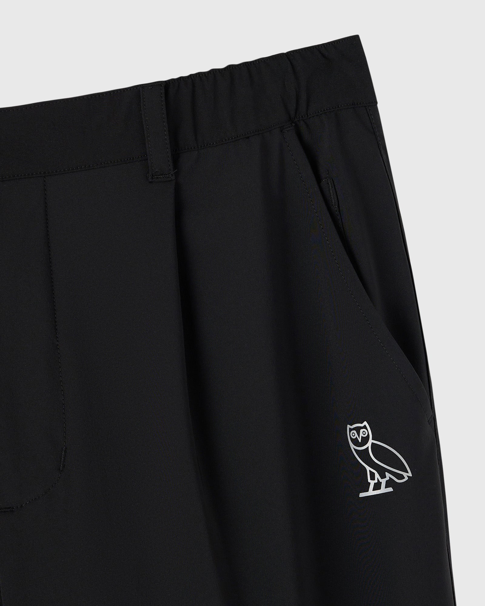 Black stretch nylon chino pants with waistband, front pockets, and OVO owl logo embroidered on thigh.
