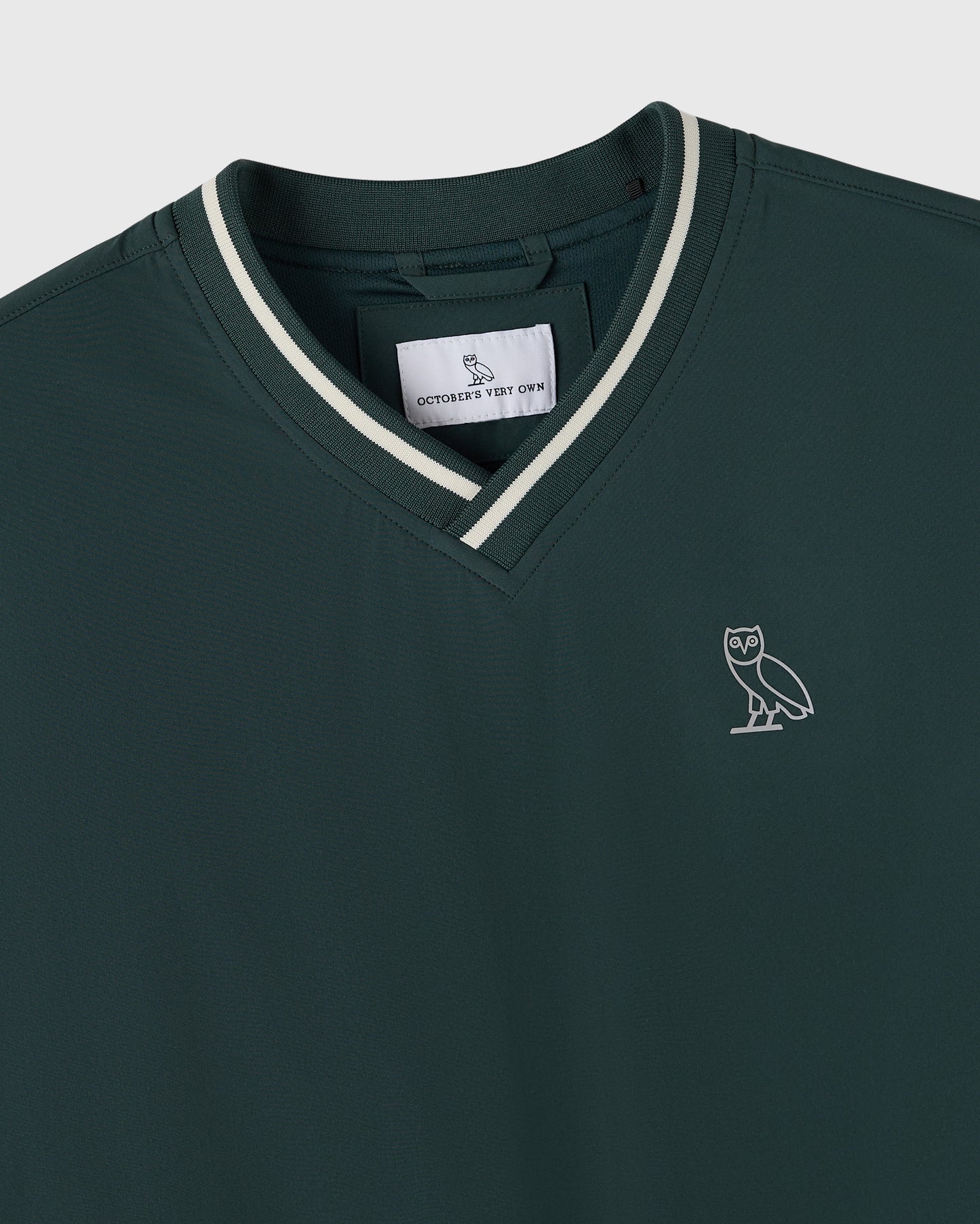 Midnight green V-neck pullover with white striping at neckline and small owl logo on chest.