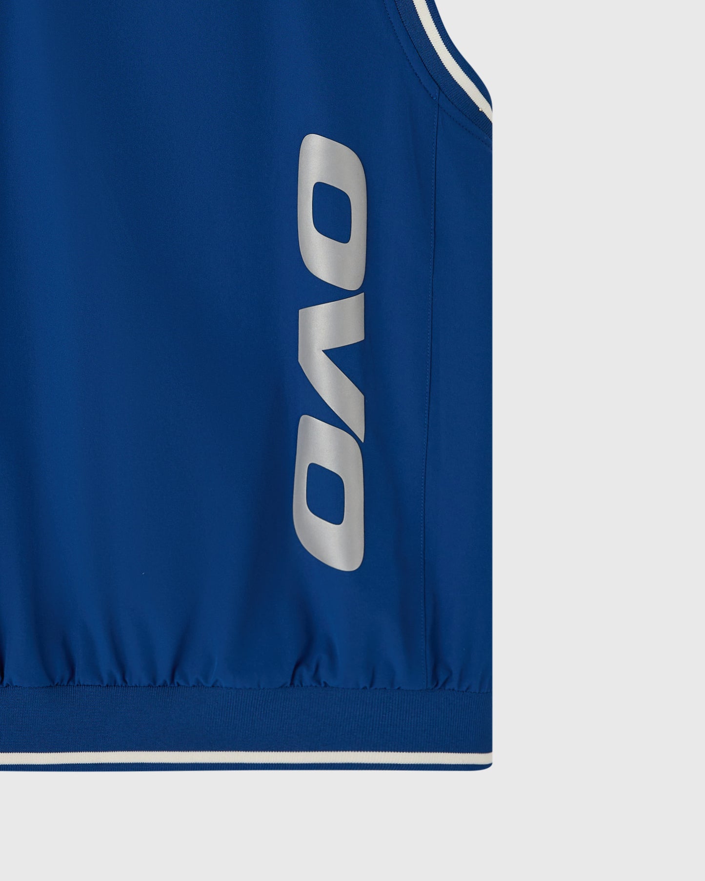 Deep denim stretch nylon pullover vest with silver OVO logo and white piping detail on armholes and hem.