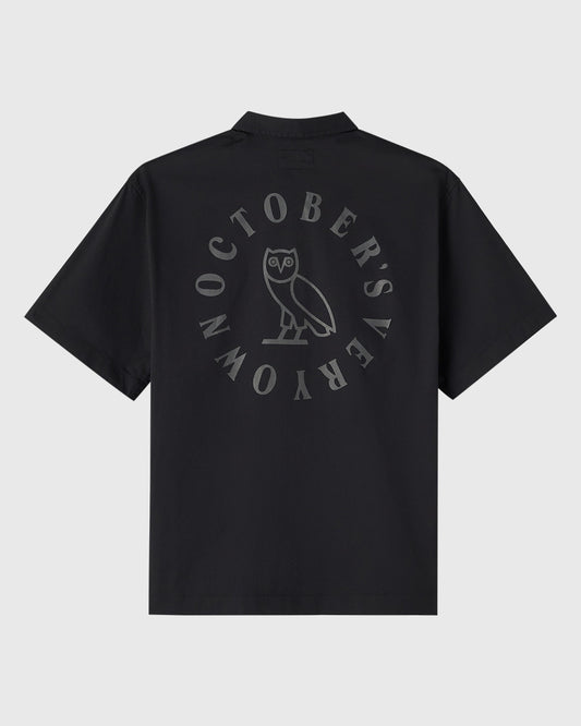 Black camp shirt with circular wordmark and owl graphic printed on back.