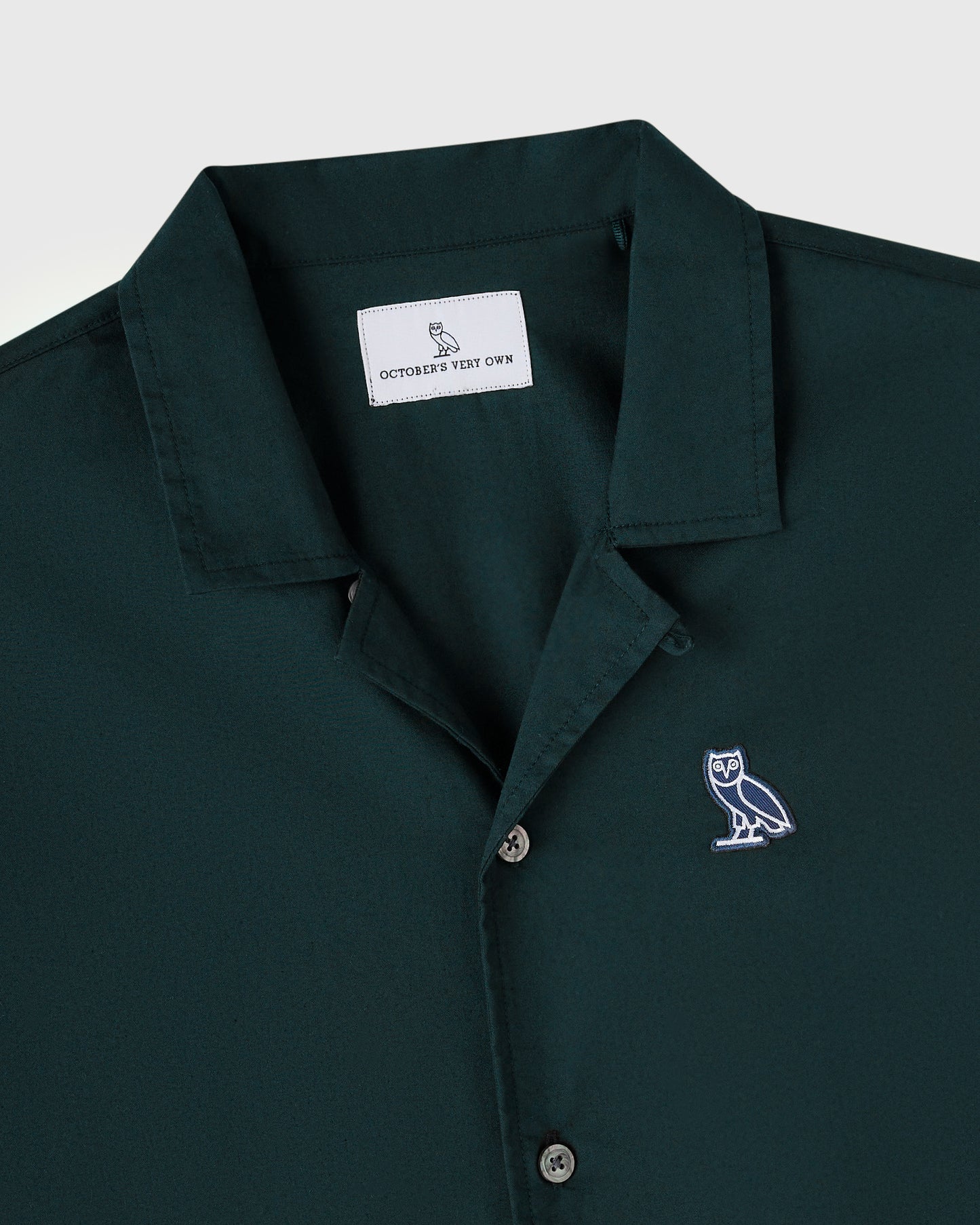 Midnight green camp shirt with owl embroidery on chest and branded neck label.