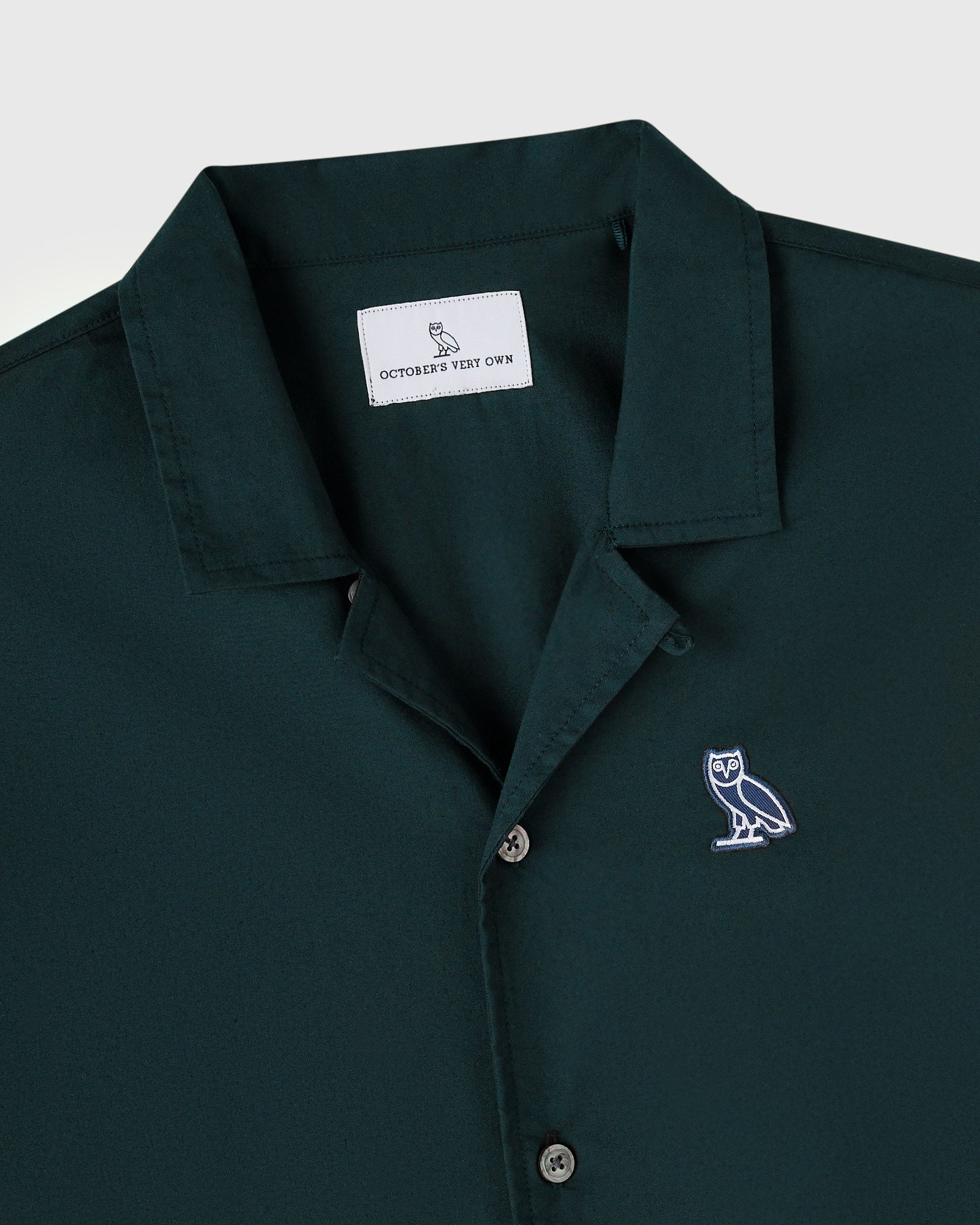 Midnight green camp shirt with owl embroidery on chest and branded neck label.