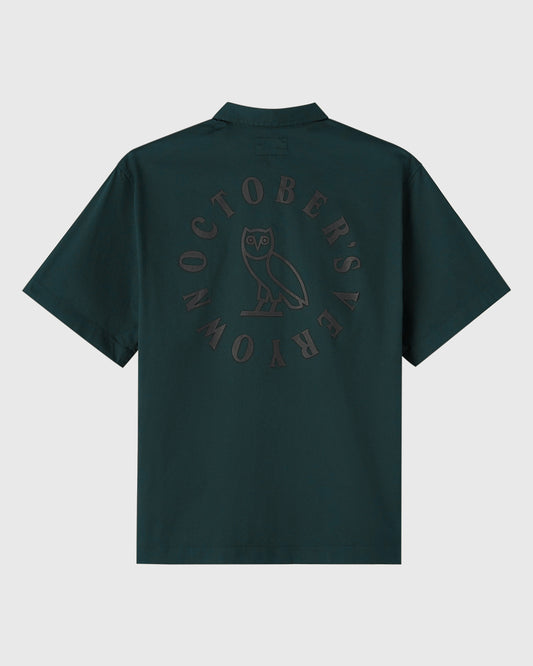 Midnight green camp shirt with circular owl wordmark graphic on back.