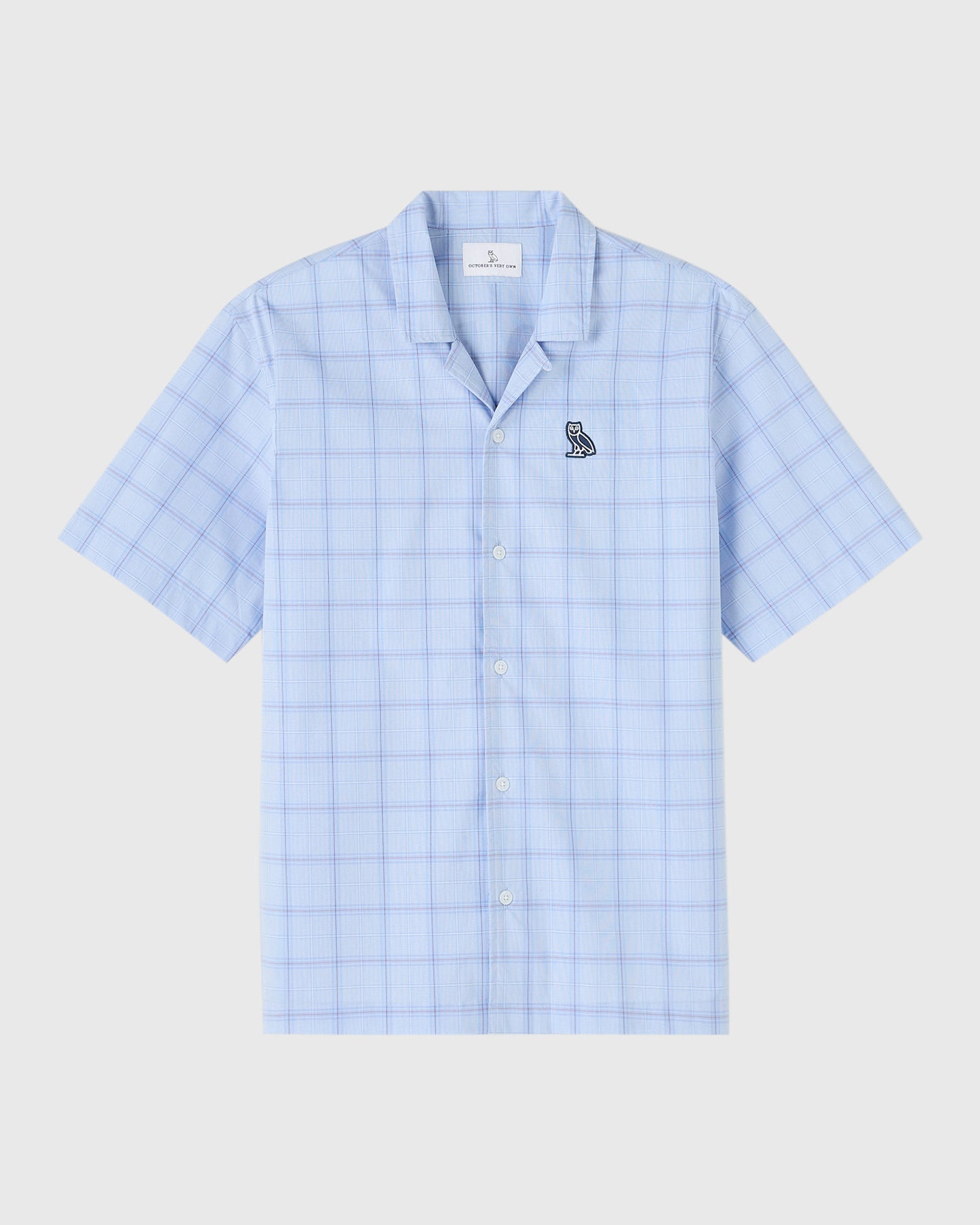 Light blue check camp shirt with short sleeves, white button front, and small circle wordmark emblem on chest.