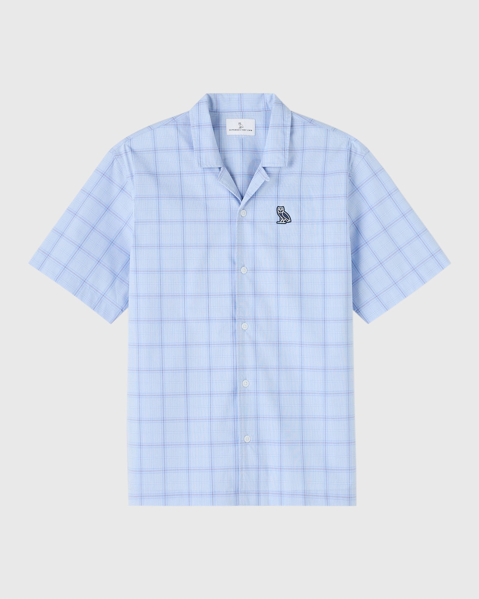 Light blue check camp shirt with short sleeves, white button front, and small circle wordmark emblem on chest.