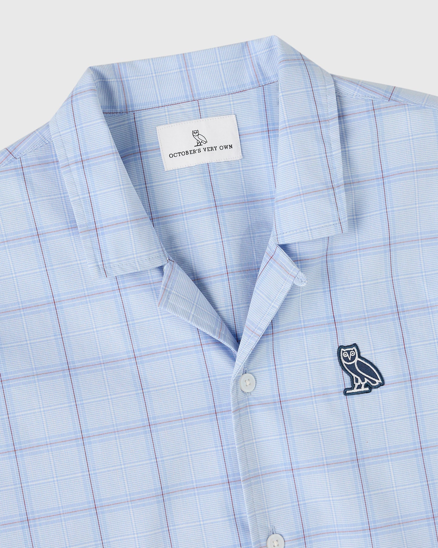 Light blue camp shirt with blue and pink plaid pattern, owl embroidery on chest, and brand label visible at collar.