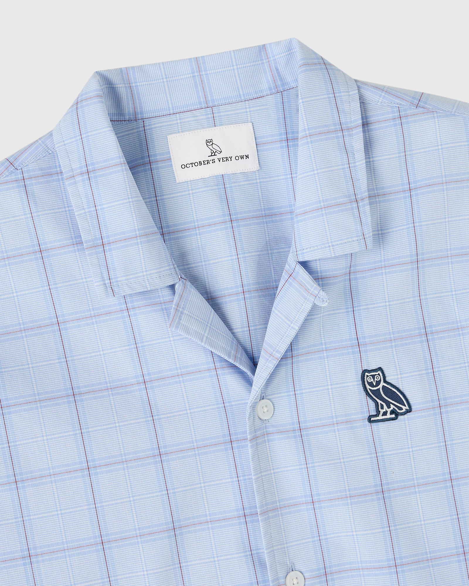 Light blue camp shirt with blue and pink plaid pattern, owl embroidery on chest, and brand label visible at collar.