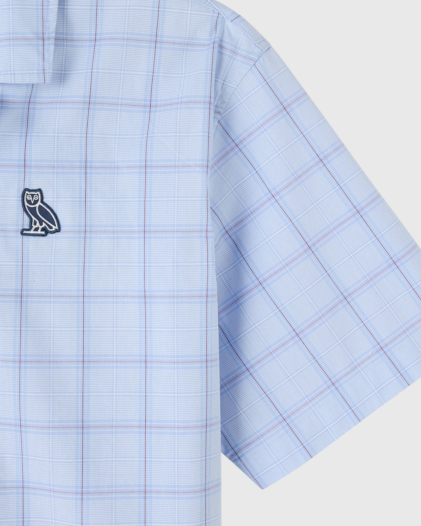 Light blue camp shirt with red and blue plaid pattern and owl logo emblem on chest.