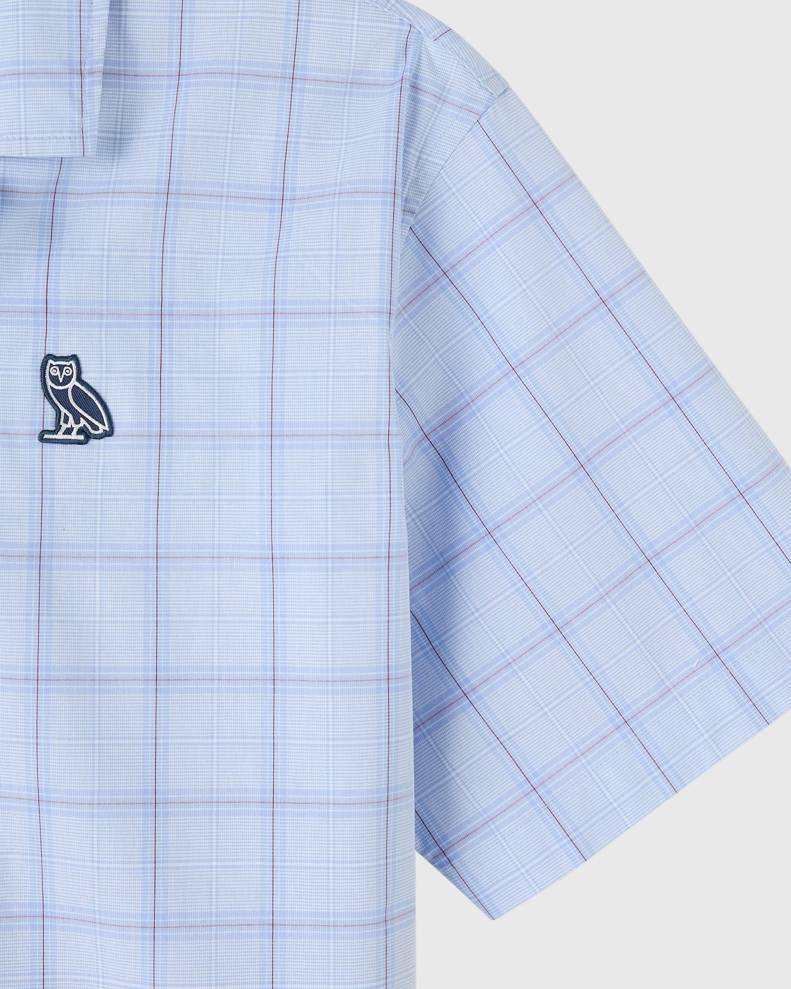 Light blue camp shirt with red and blue plaid pattern and owl logo emblem on chest.
