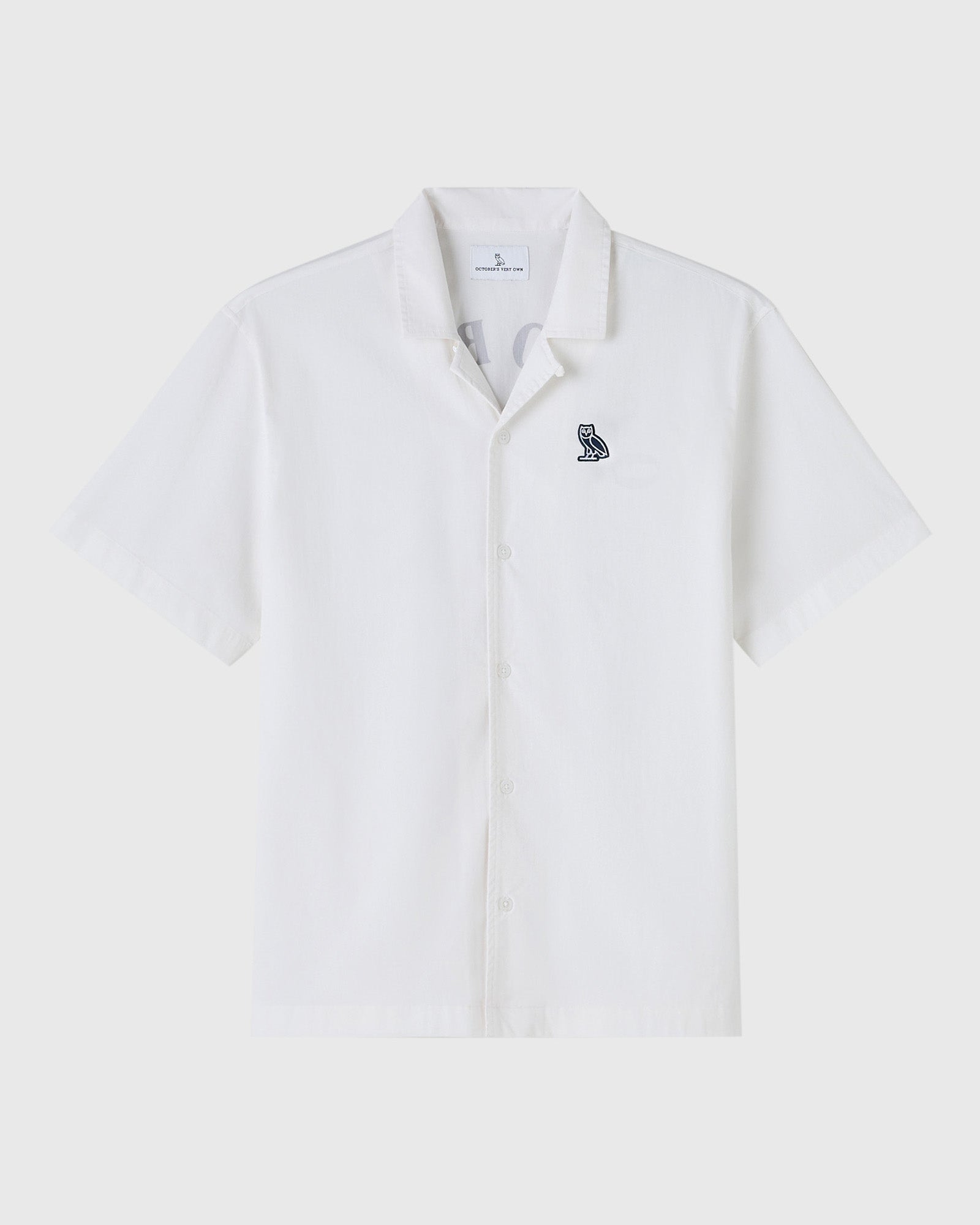 White short-sleeve camp shirt with small embroidered owl logo on chest and button front closure.
