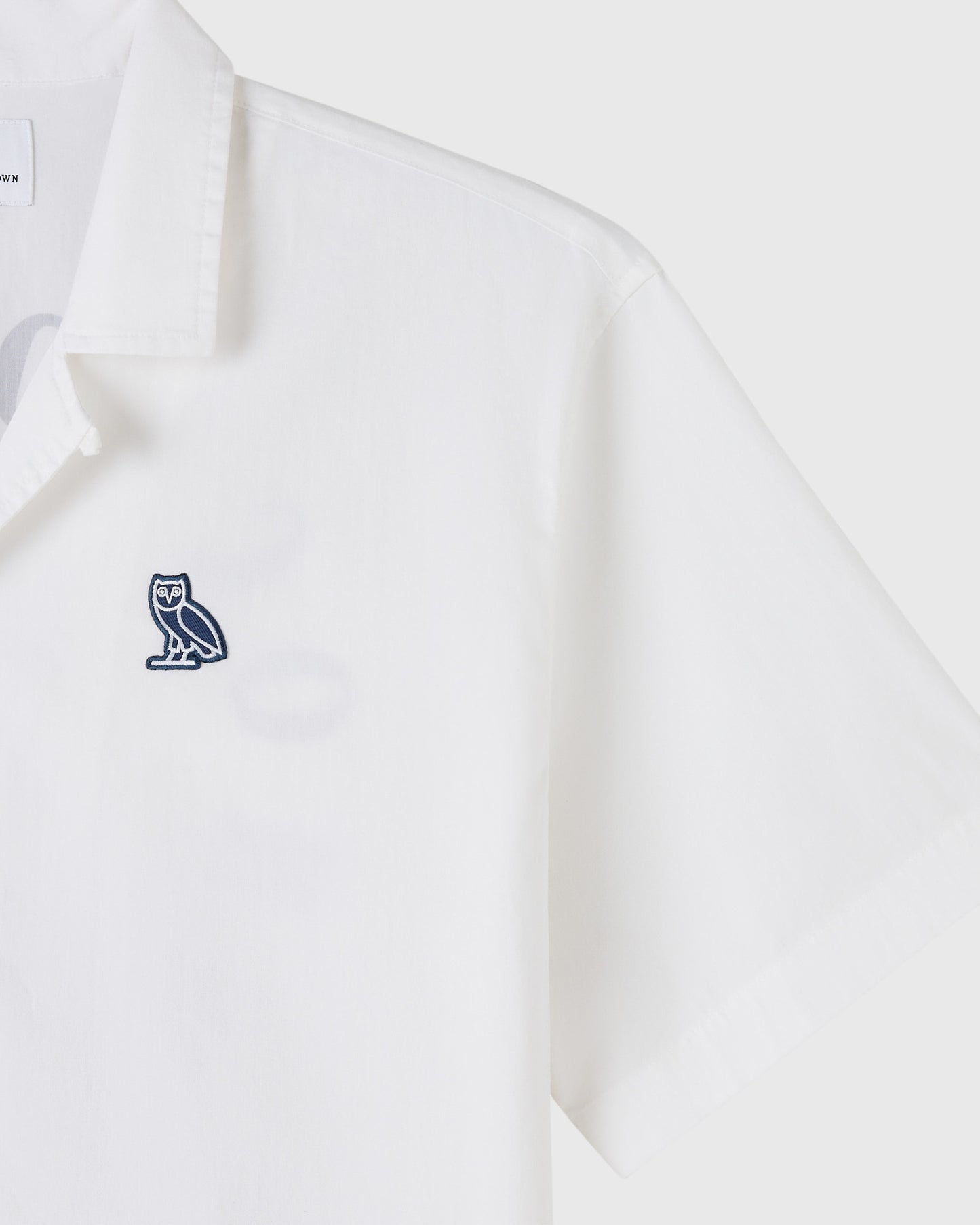 White camp shirt with small navy owl emblem on chest.