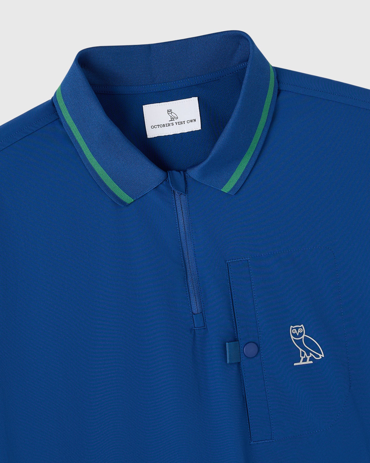 Deep denim blue polo shirt with green collar trim, chest pocket, and embroidered owl logo.