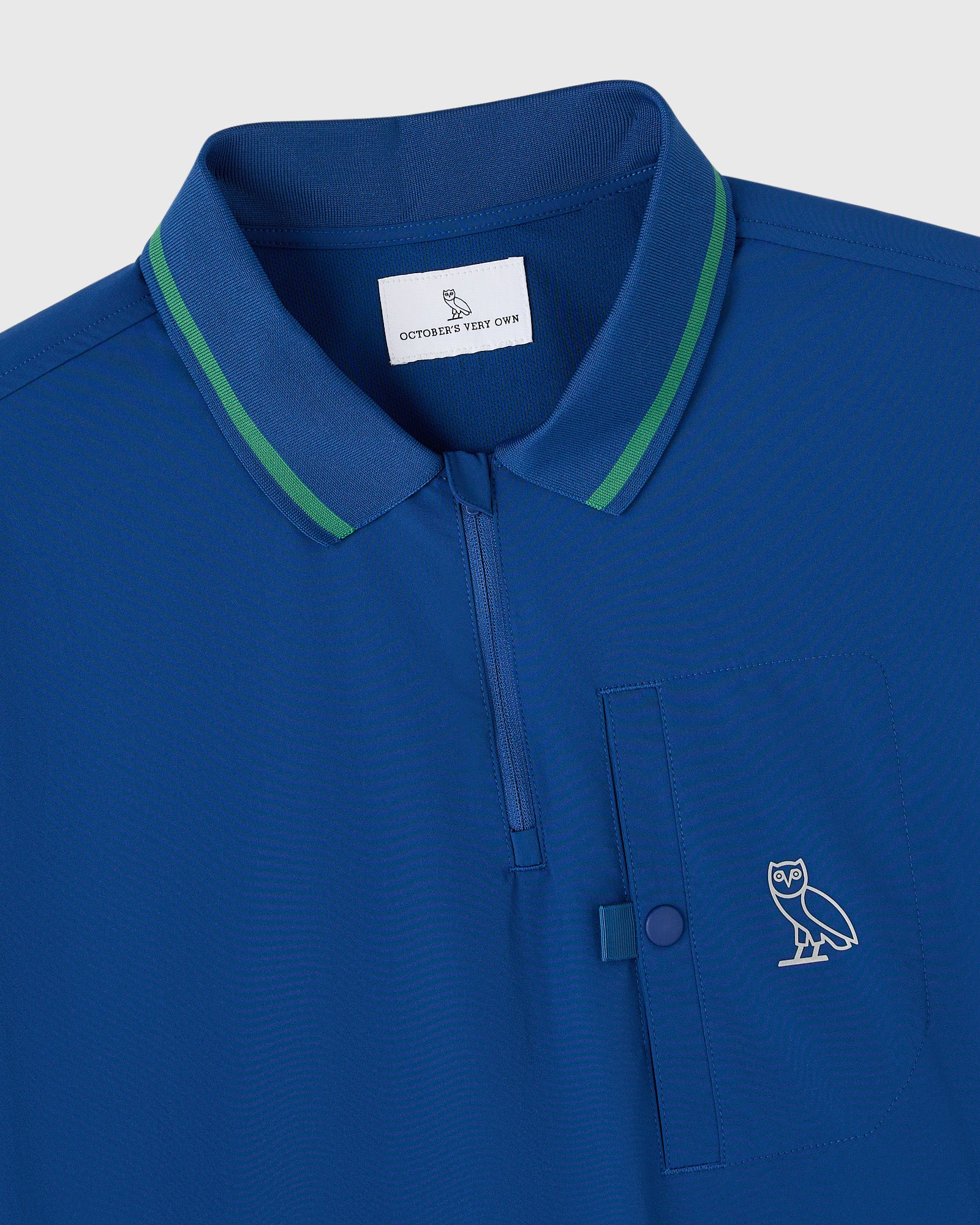 Deep denim blue polo shirt with green collar trim, chest pocket, and embroidered owl logo.