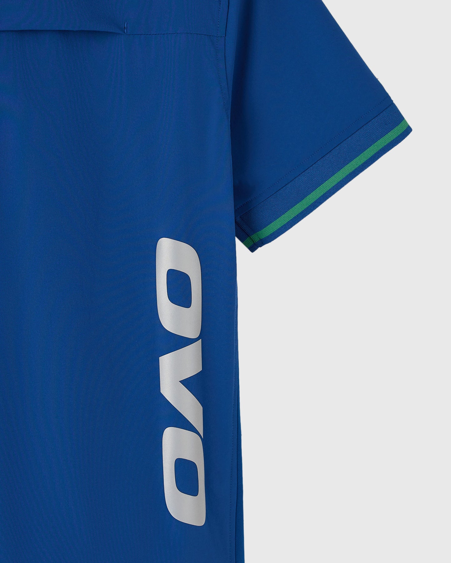 Deep denim polo shirt with white OVO logo on chest, green and navy stripe on sleeve cuff.