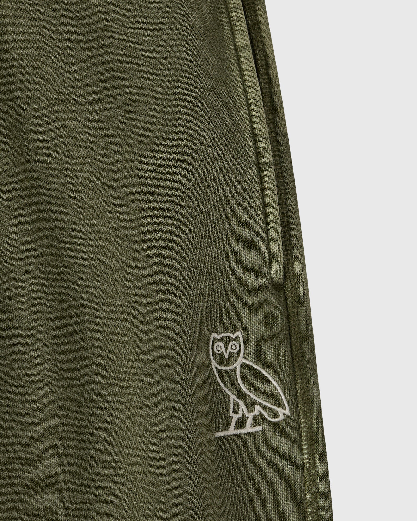 Cypress green sweatpant with ribbed texture and small white owl embroidery on leg.