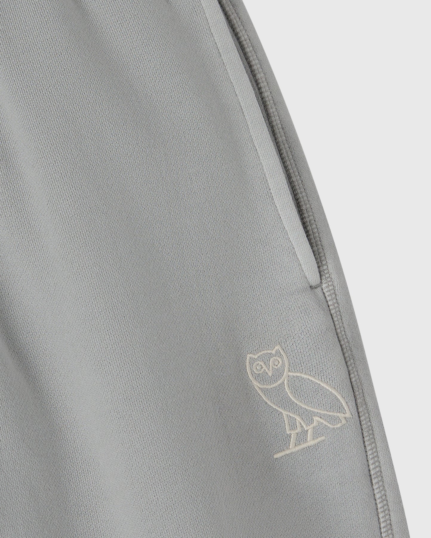 Gray sweatpant with open hem and owl embroidery on the leg.