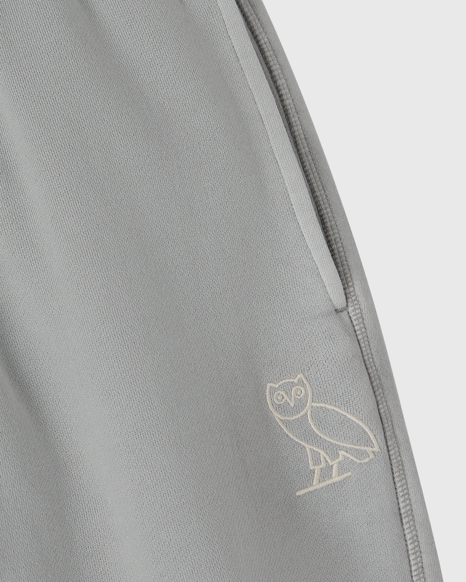 Gray sweatpant with open hem and owl embroidery on the leg.
