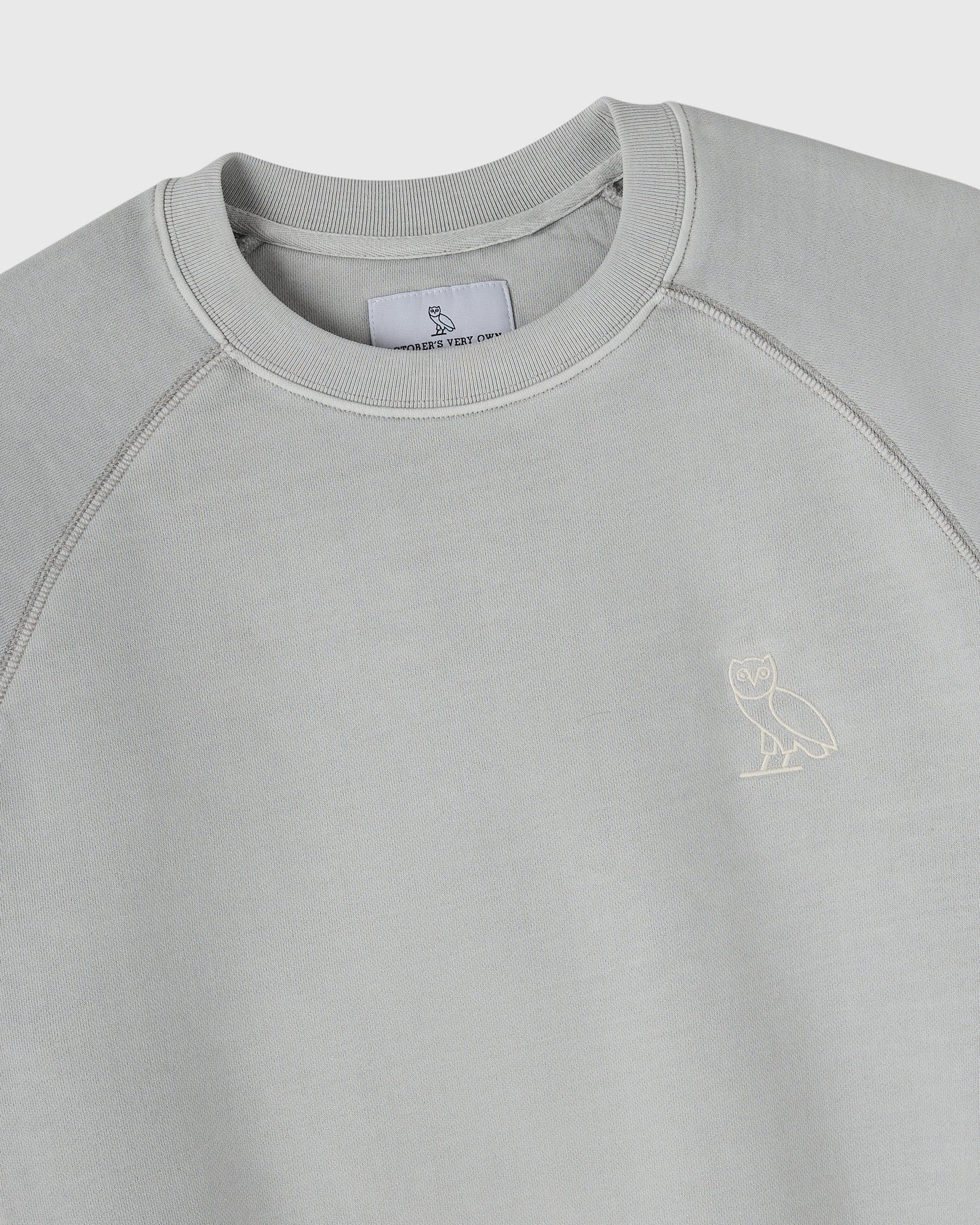 Gray crewneck sweatshirt with ribbed collar, raglan sleeves, and small owl embroidery on chest.