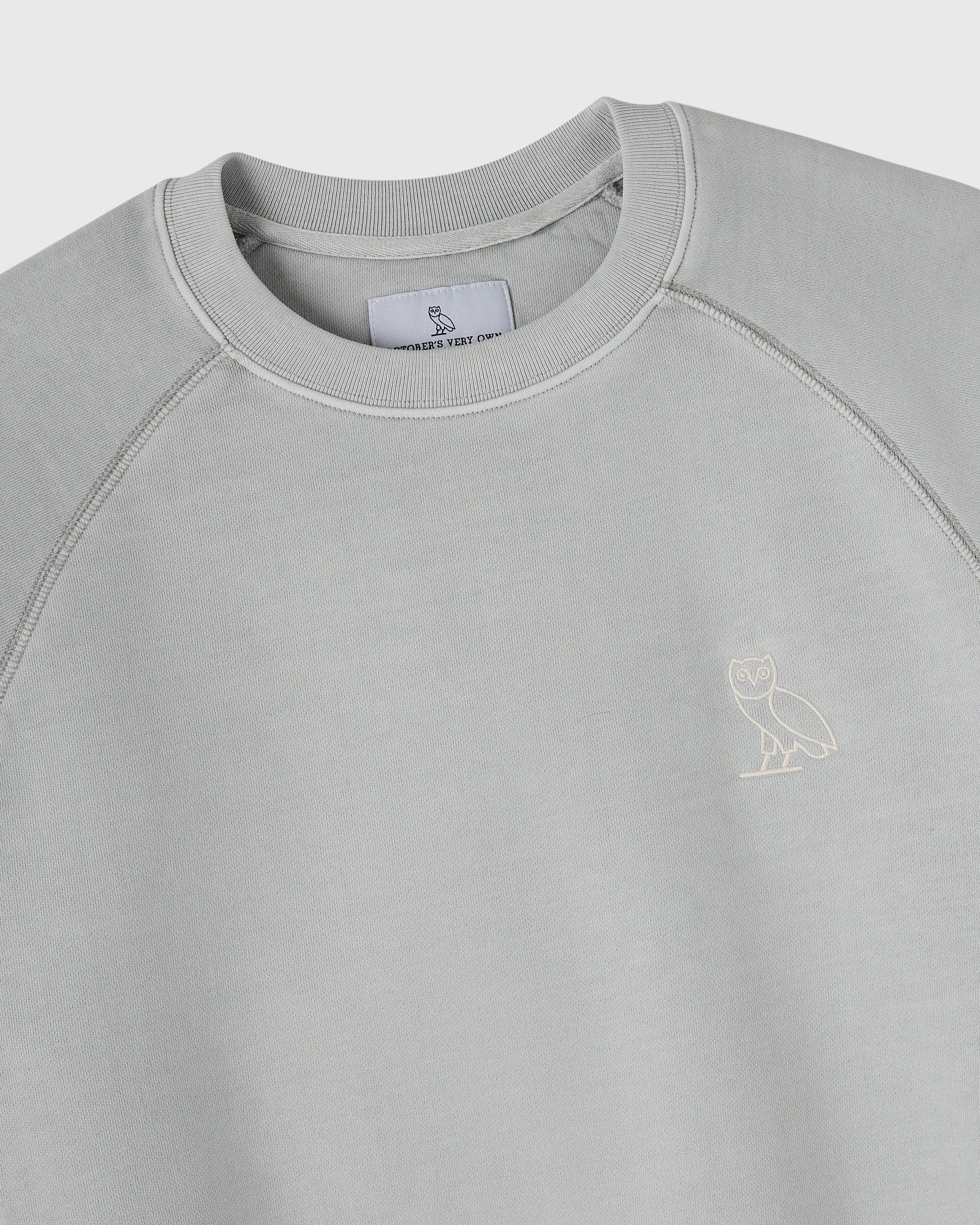 Gray crewneck sweatshirt with ribbed collar, raglan sleeves, and small owl embroidery on chest.