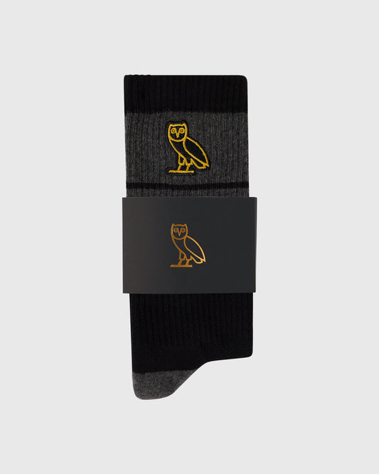 Black crew socks with gold owl embroidery, folded and displayed with black packaging band.