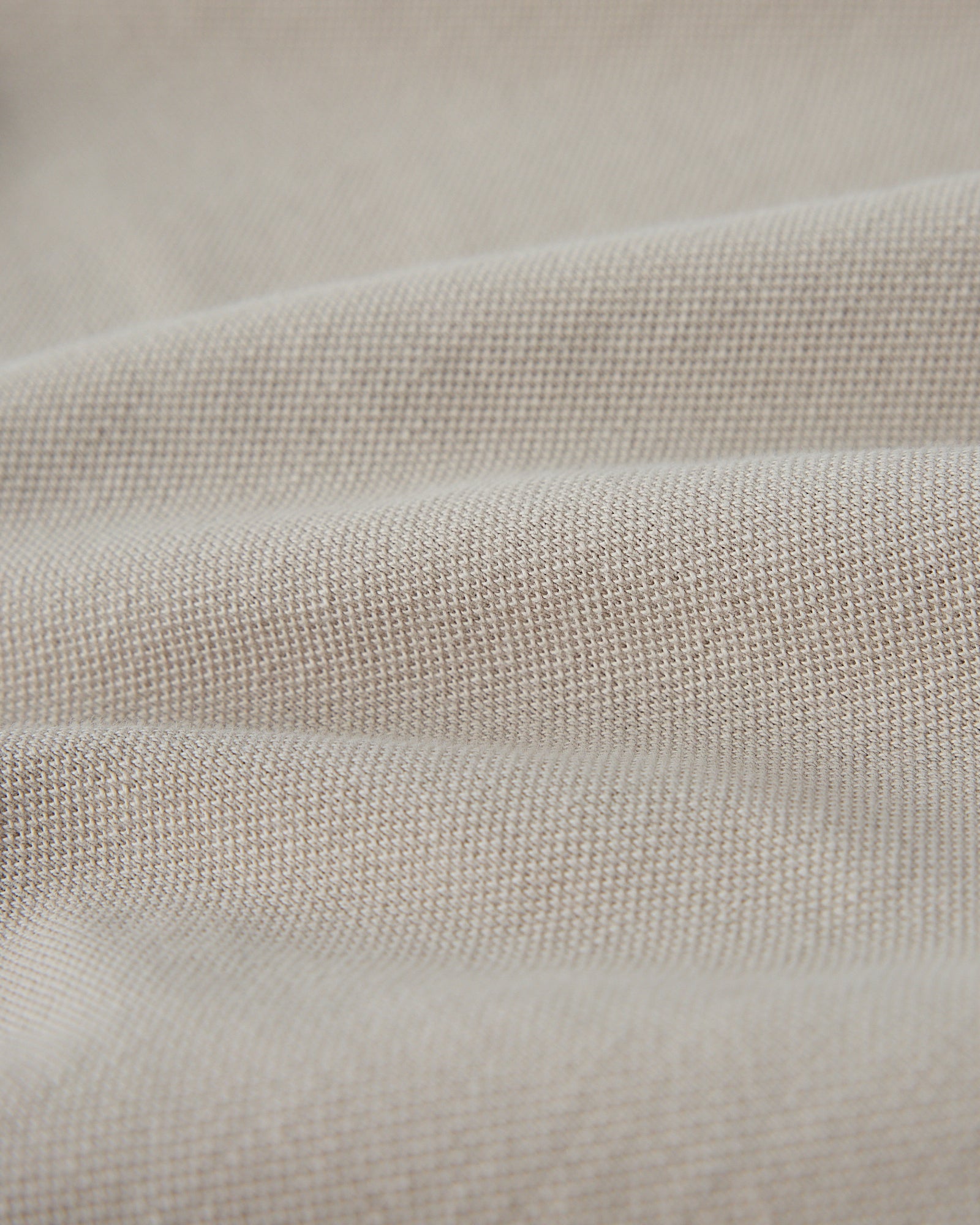 Close-up of sandstone-colored polo fabric showing textured knit weave.