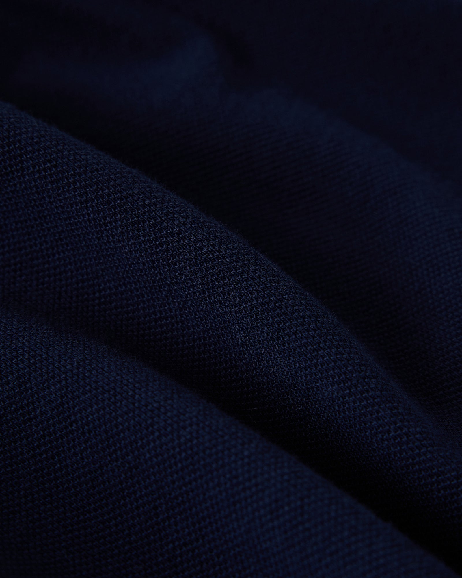 Navy blue polo shirt fabric with ribbed knit texture and diagonal fold detail.