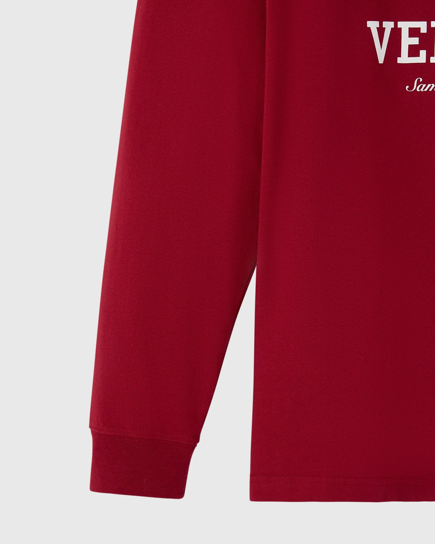 Deep red long-sleeve tee with white text and ribbed cuffs, shown from torso detail.