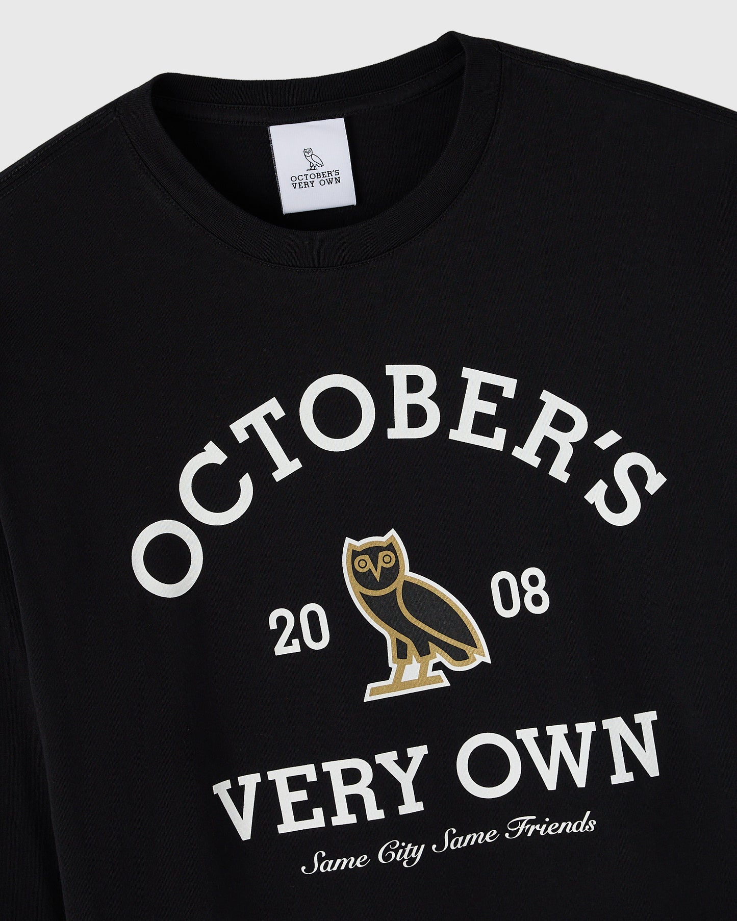 Black long-sleeve tee with white "October's Very Own" text, gold owl graphic, and "Same City Same Friends" slogan.