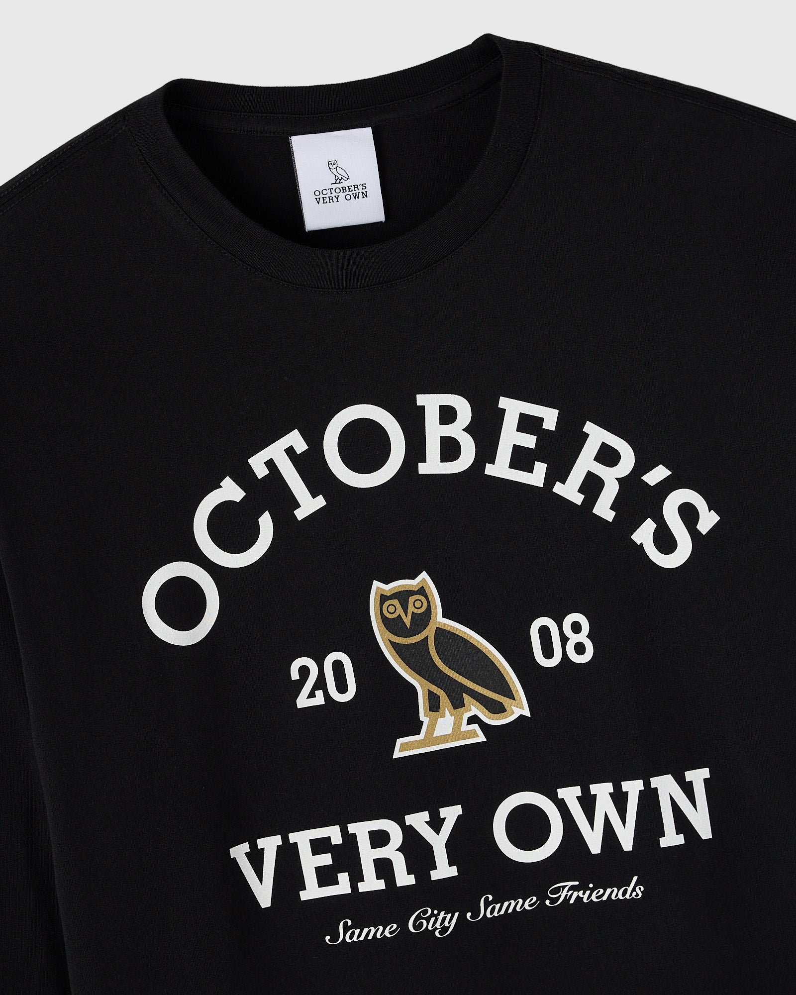 Black long-sleeve tee with white "October's Very Own" text, gold owl graphic, and "Same City Same Friends" slogan.