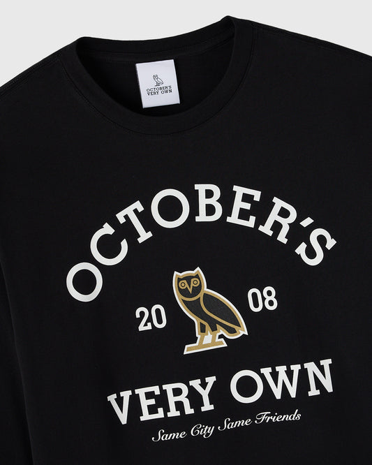 Black long-sleeve tee with white "October's Very Own" text, gold owl graphic, and "Same City Same Friends" slogan.