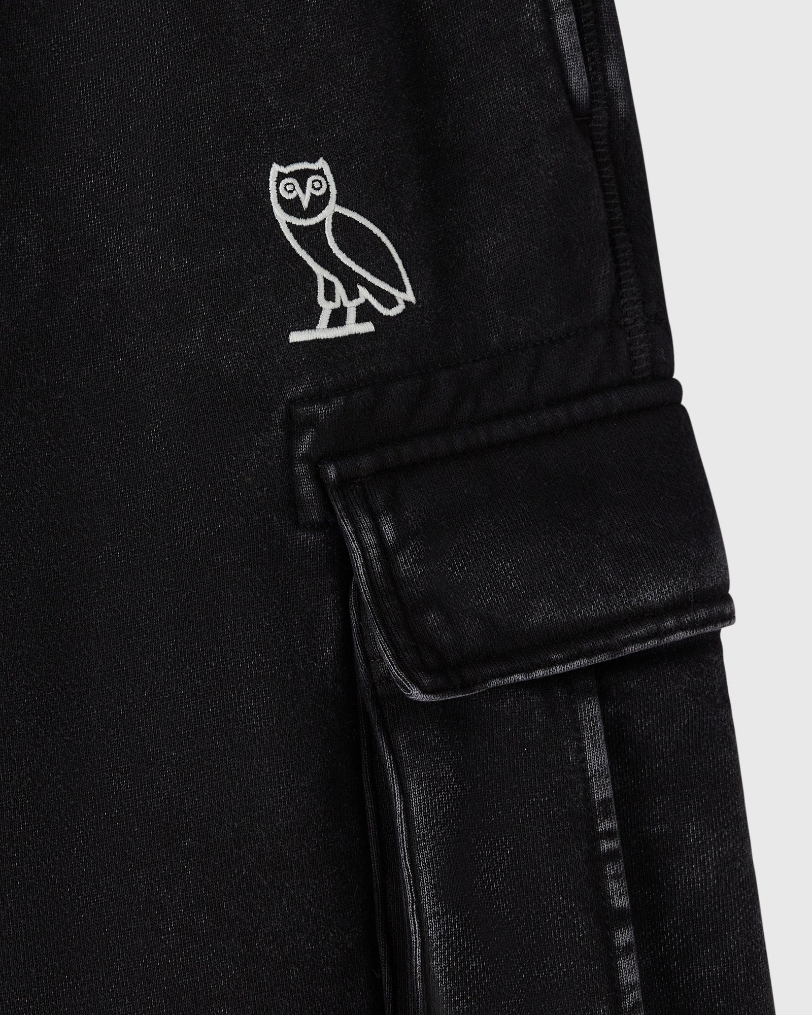 Black cargo sweatpant with white owl embroidery on chest and flap pocket on thigh.