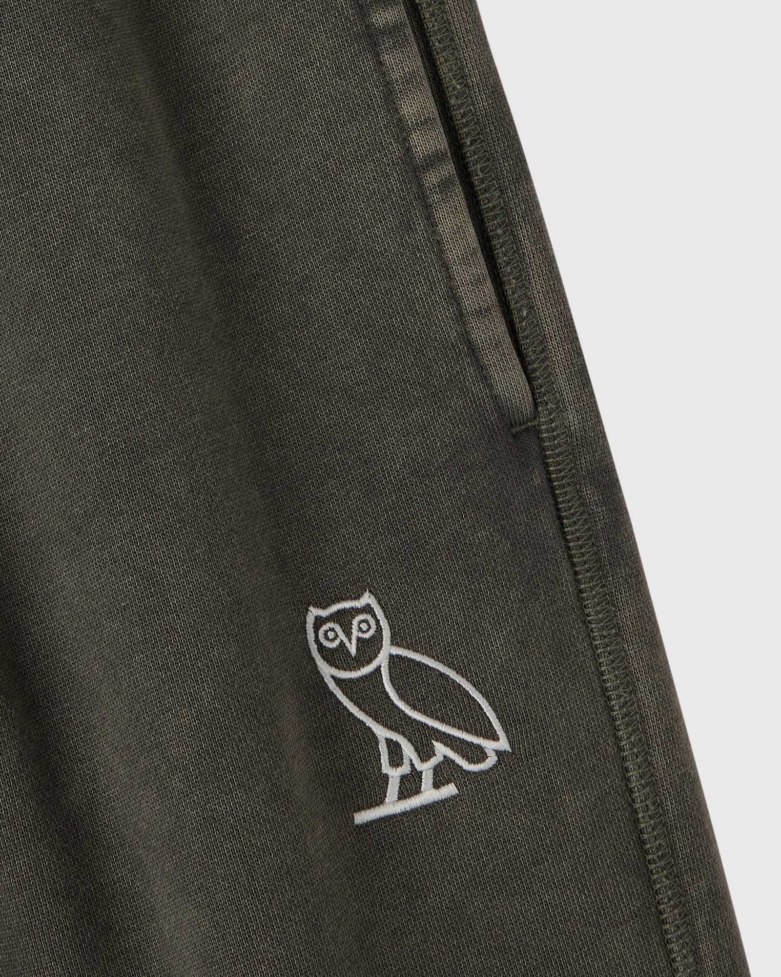 Deep olive sweatpant with white owl embroidery on thigh and side seam detail.
