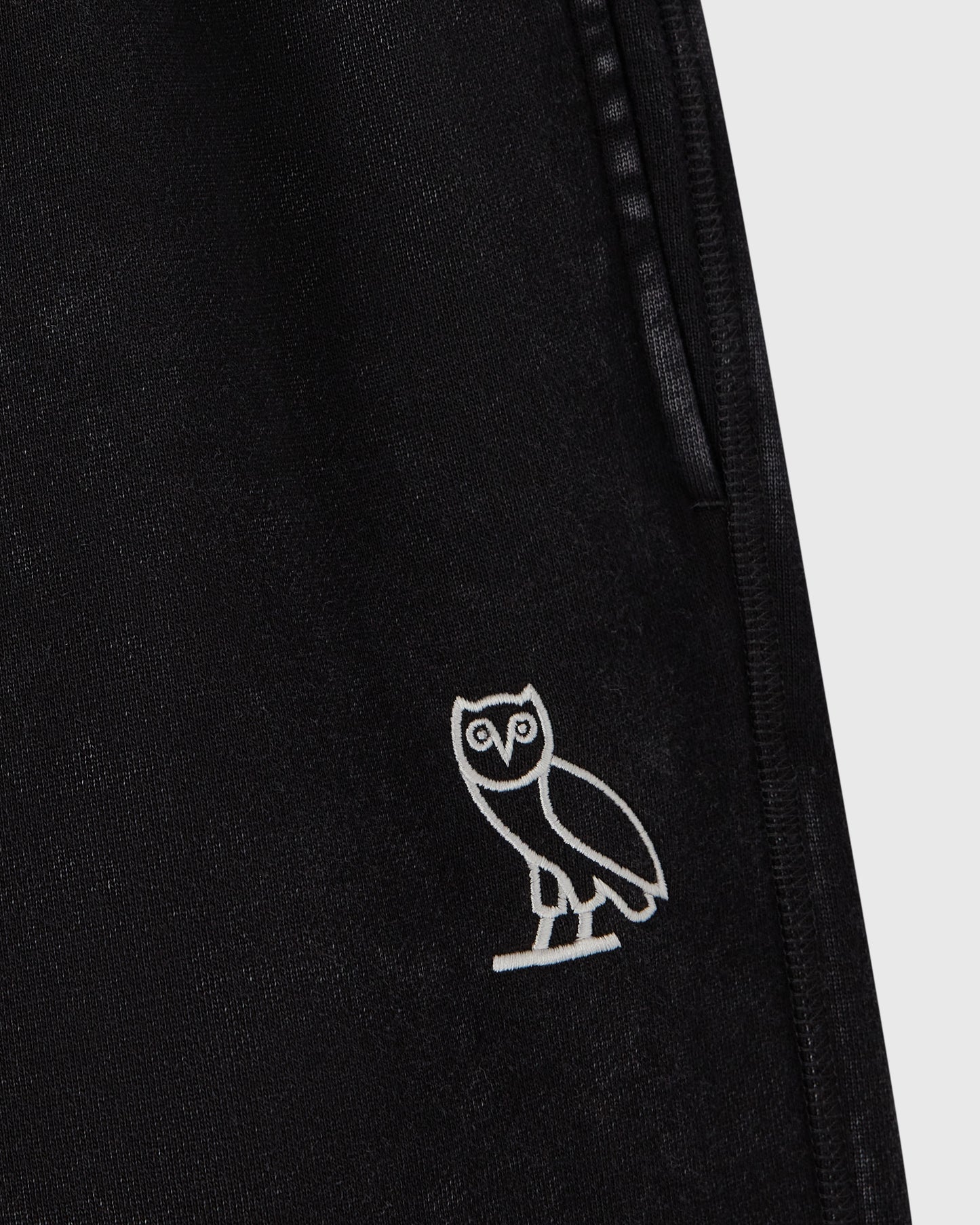 Black sweatpants with white owl embroidery on leg and side seam detail.