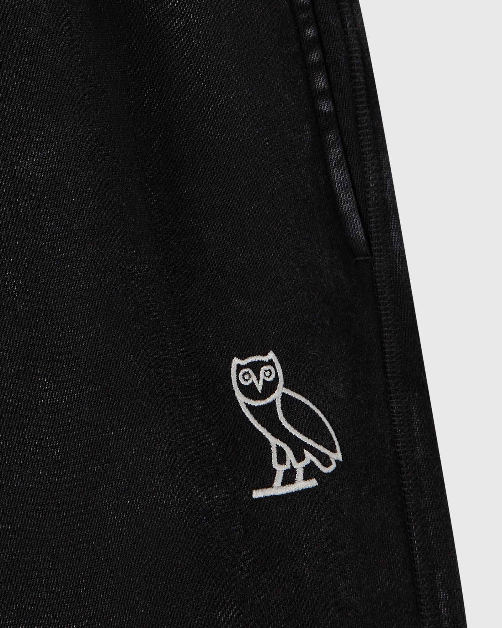 Black sweatpants with white owl embroidery on leg and side seam detail.