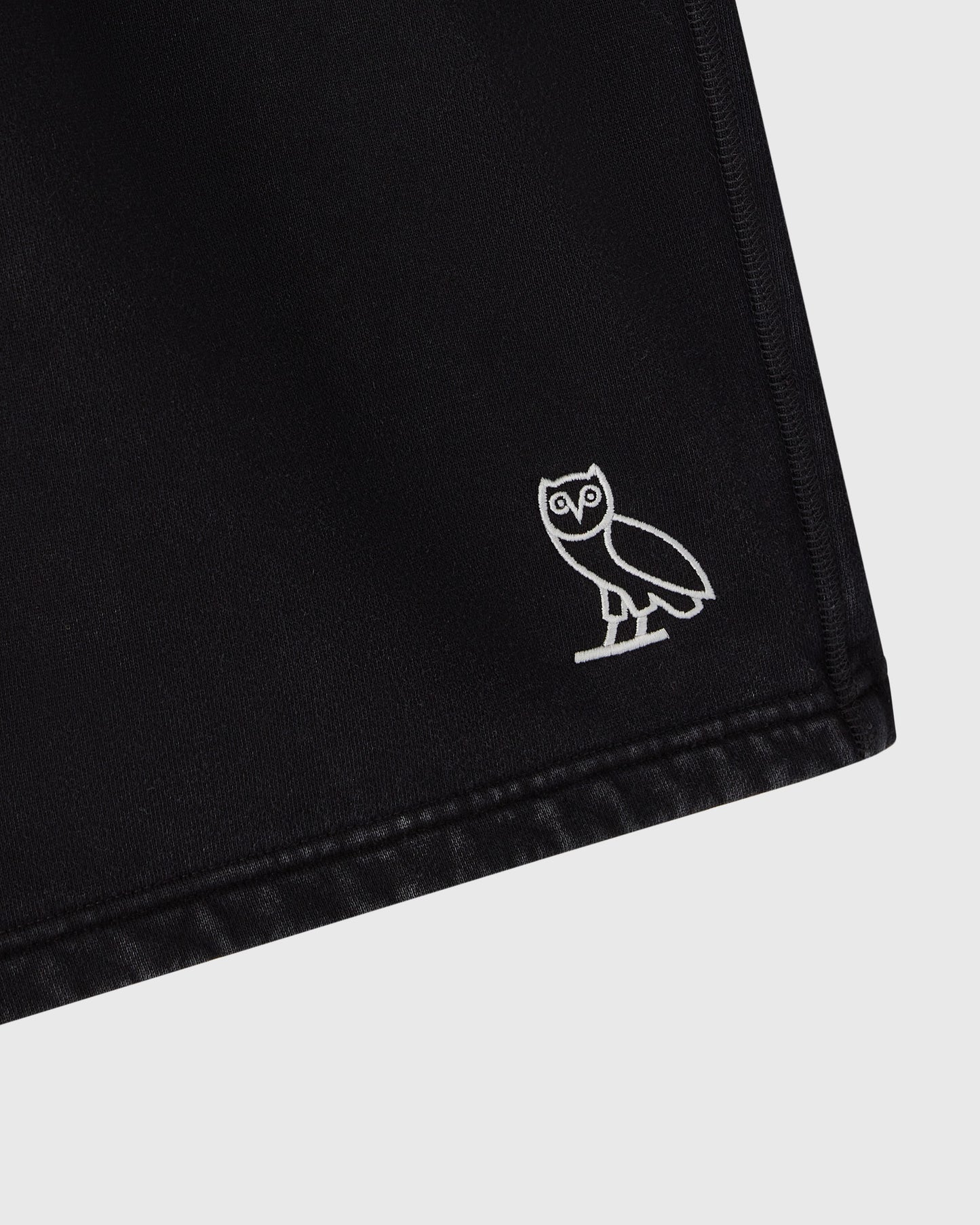 Black sweatshorts with white owl embroidery on the leg and stitched hem detail.