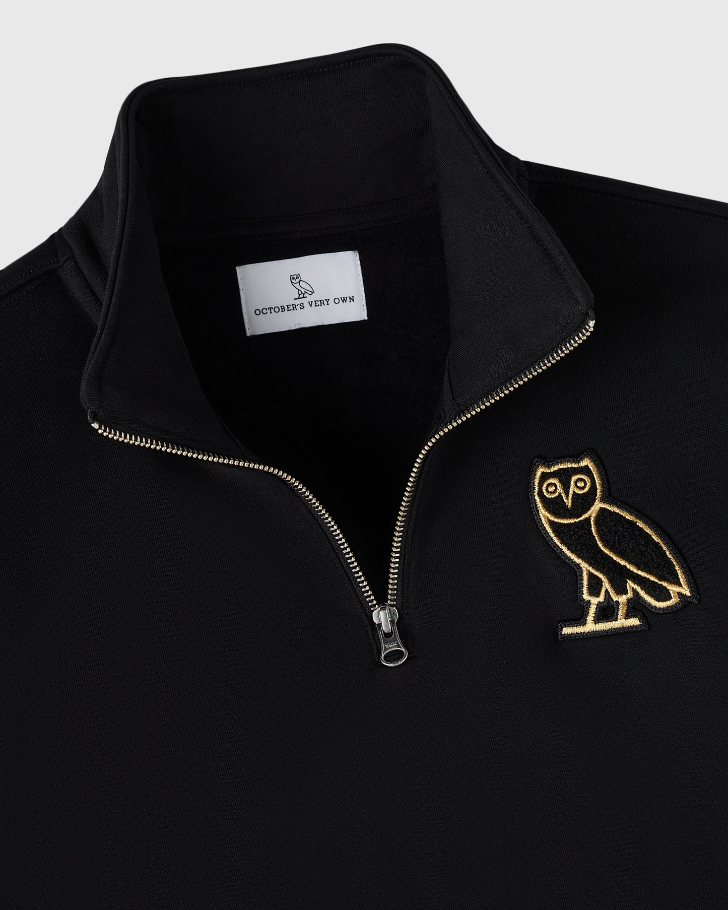 Black quarter-zip mockneck with gold embroidered owl on chest and metal slider zipper.