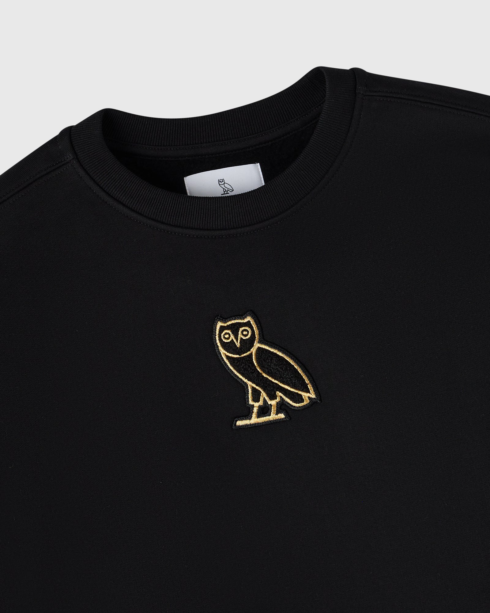Black crewneck sweatshirt with gold owl embroidery on chest and brand label at neckline.