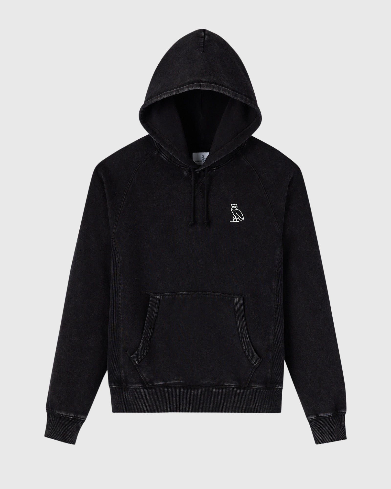 Black raglan hoodie with garment-dyed finish, drawstring hood, kangaroo pocket, and small owl embroidery on chest.