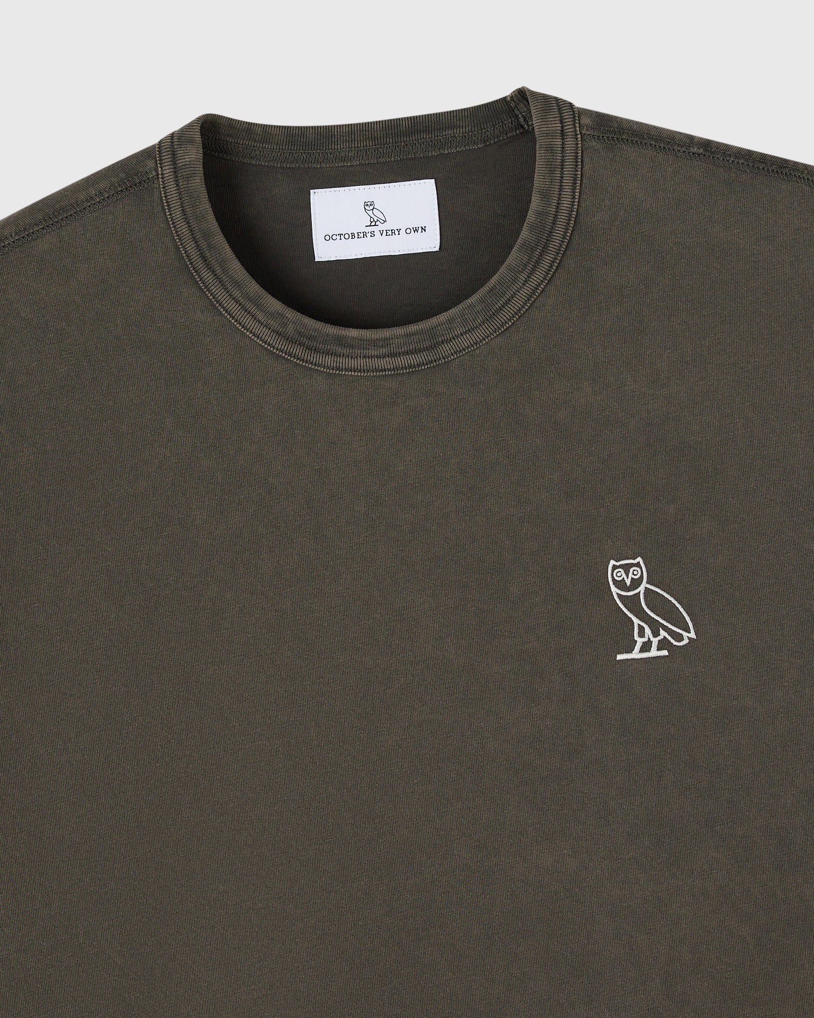 Deep olive crewneck t-shirt with small white owl embroidery on chest and brand label at neckline.