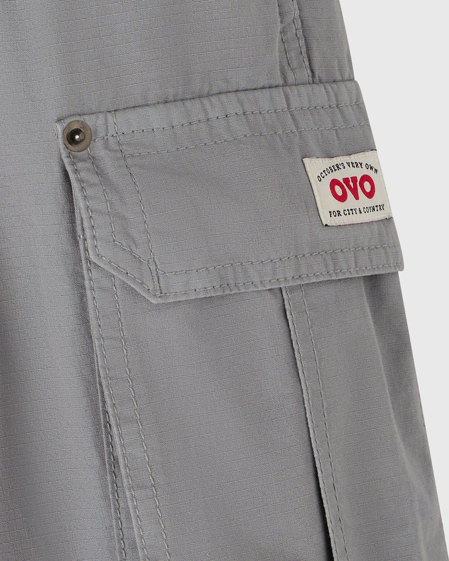 Grey cargo pants with multiple pockets and brass button closures on thigh pocket flaps.