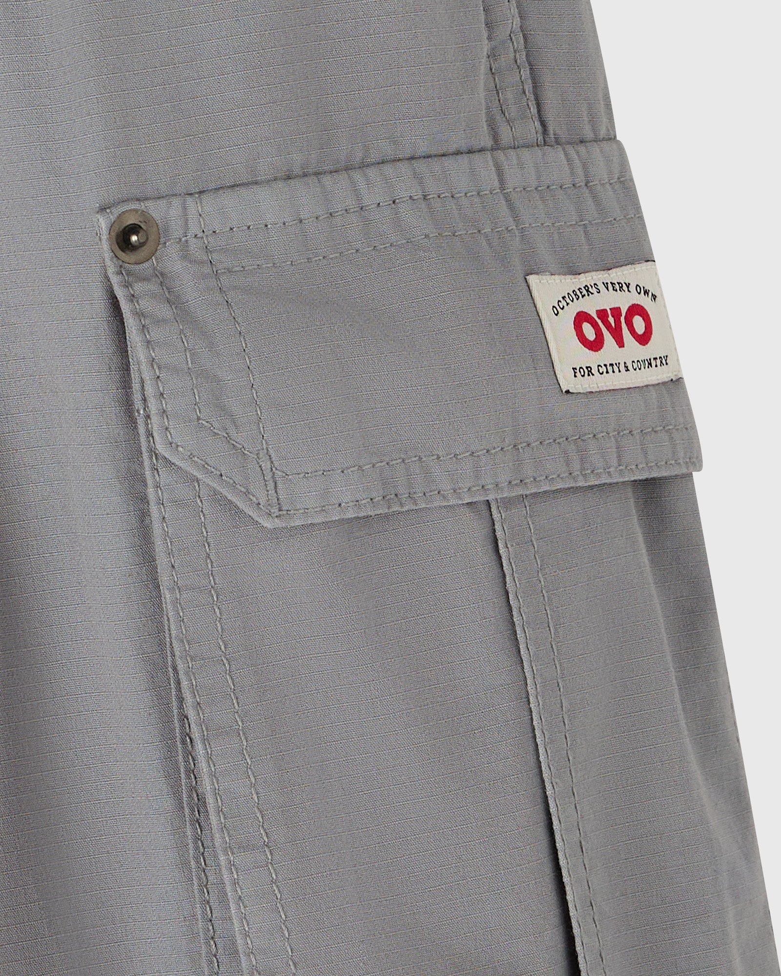 Grey cargo pants with multiple pockets and brass button closures on thigh pocket flaps.