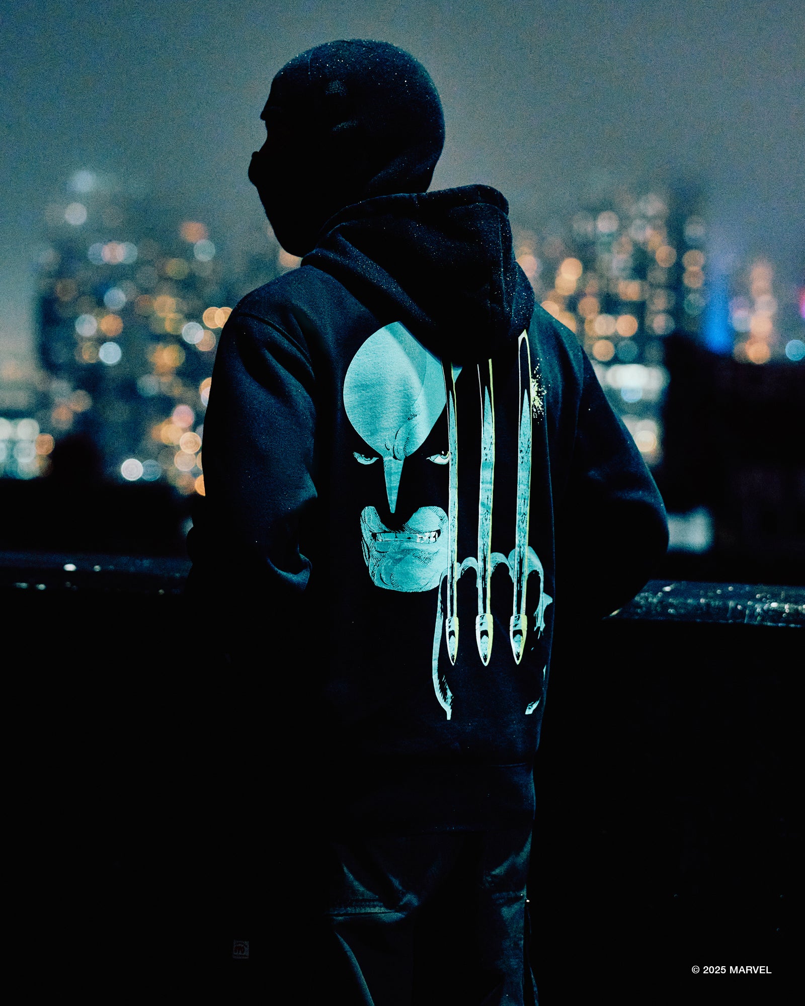 Person wearing a October’s Very Own hoodie with a glowing superhero emblem against a cityscape at night