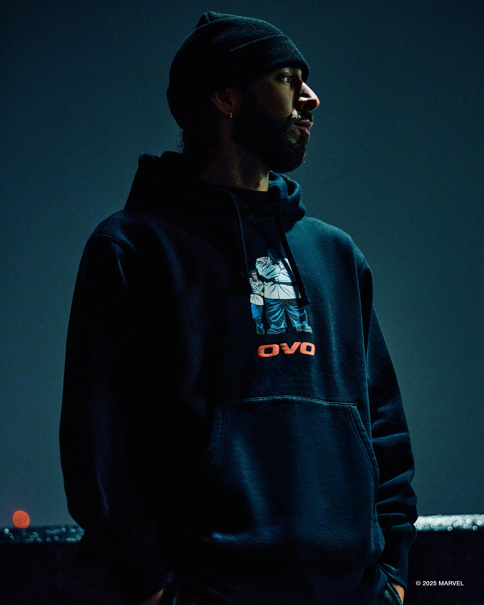 Person wearing a dark October’s Very Own hoodie with a graphic design on a dark background