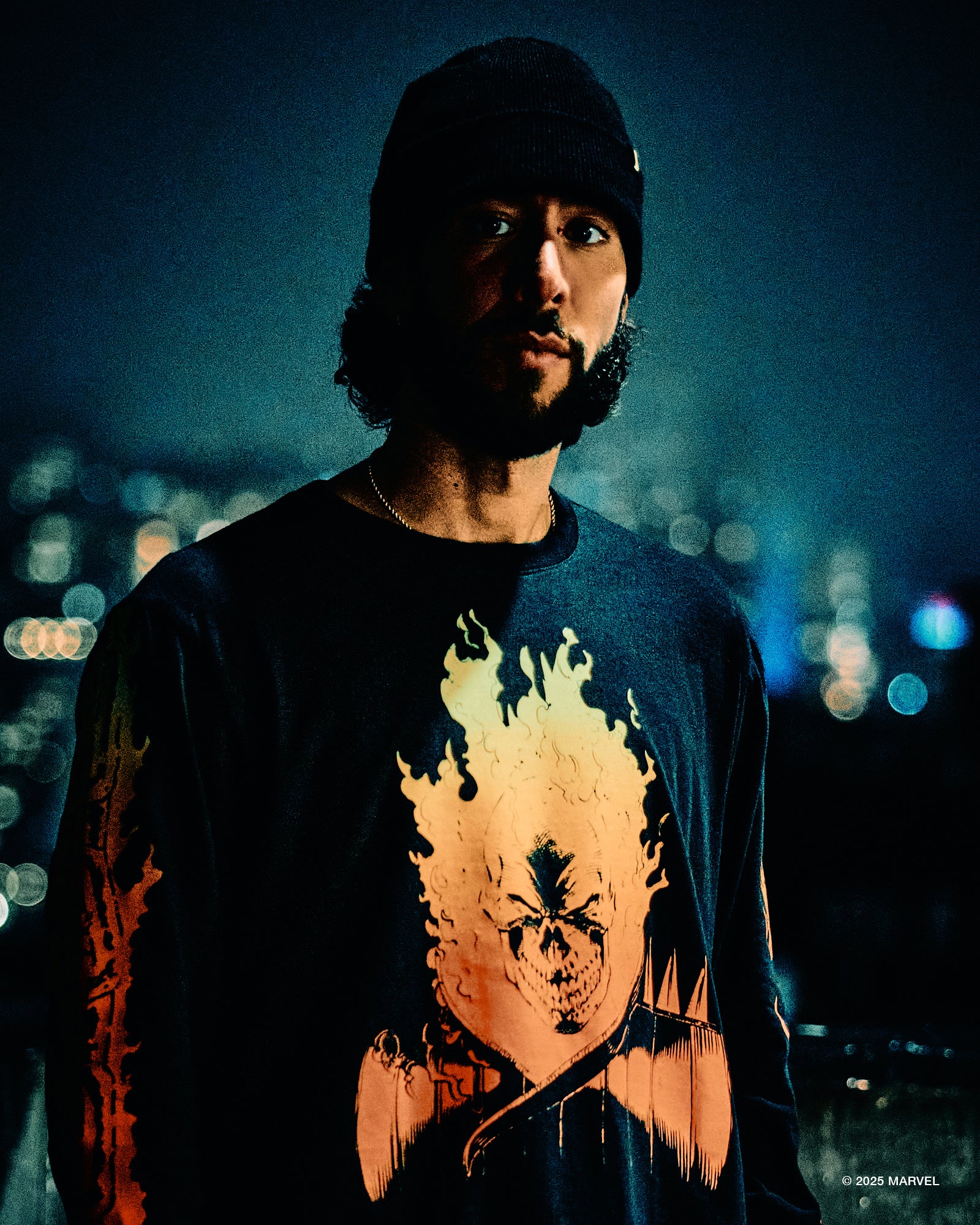 Person wearing a black October’s Very Own t-shirt with a graphic design, standing against a night-time cityscape background.