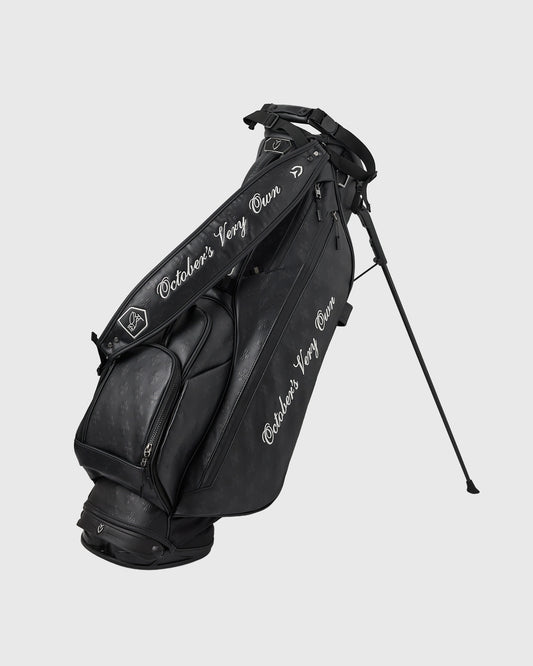 Black Vessel golf stand bag with monogram text on front panel and shoulder strap, featuring kickstand legs extended.
