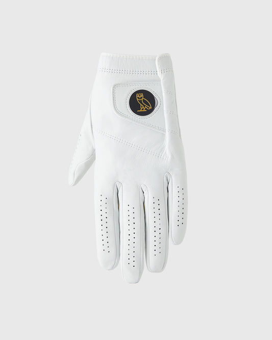 White golf glove with perforated fingers, circular logo patch on back, and ribbed wrist cuff.